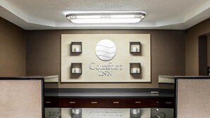 Un área de recepción con un cartel que dice "Comfort Inn" y un diseño moderno con acabado en madera clara y decoración minimalista.