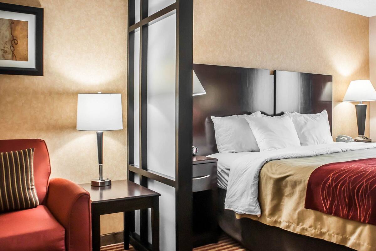 A hotel room with a bed, bedside tables, a desk, a chair, and a lamp.