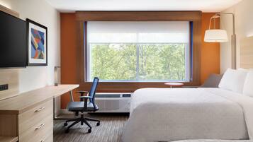 A hotel room with a bed, desk, chair, and a large window with a view of trees.
