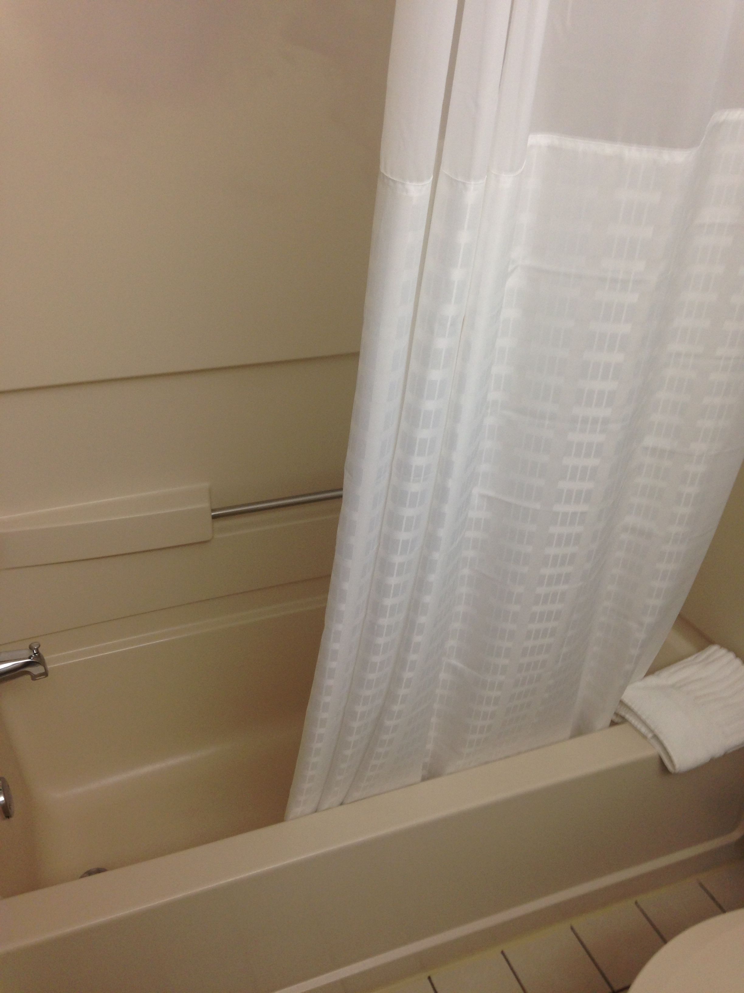 A bathtub with a white shower curtain and a towel on the side.