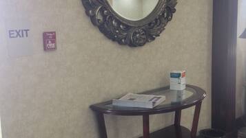 A hotel lobby with an ornate mirror, a small table with a box, an exit sign, and a potted plant.