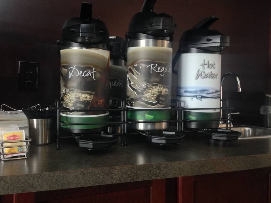 Una encimera de cocina con tres cafeteras etiquetadas 'Decaf', 'Regular' y 'Agua Caliente'.