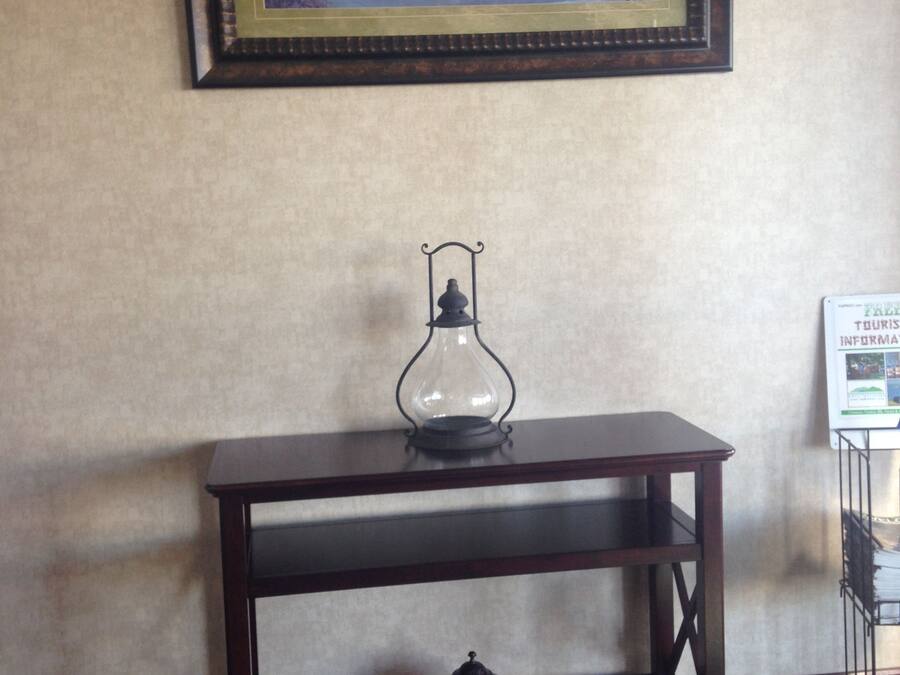 Een houten tafel met een glazen lamp en een decoratief object op het onderste plankje, een lijst met een schilderij aan de muur, en een bord met tekst aan de rechterkant.