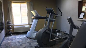 Un gimnasio con cintas de correr, bicicletas estáticas y un banco de pesas.