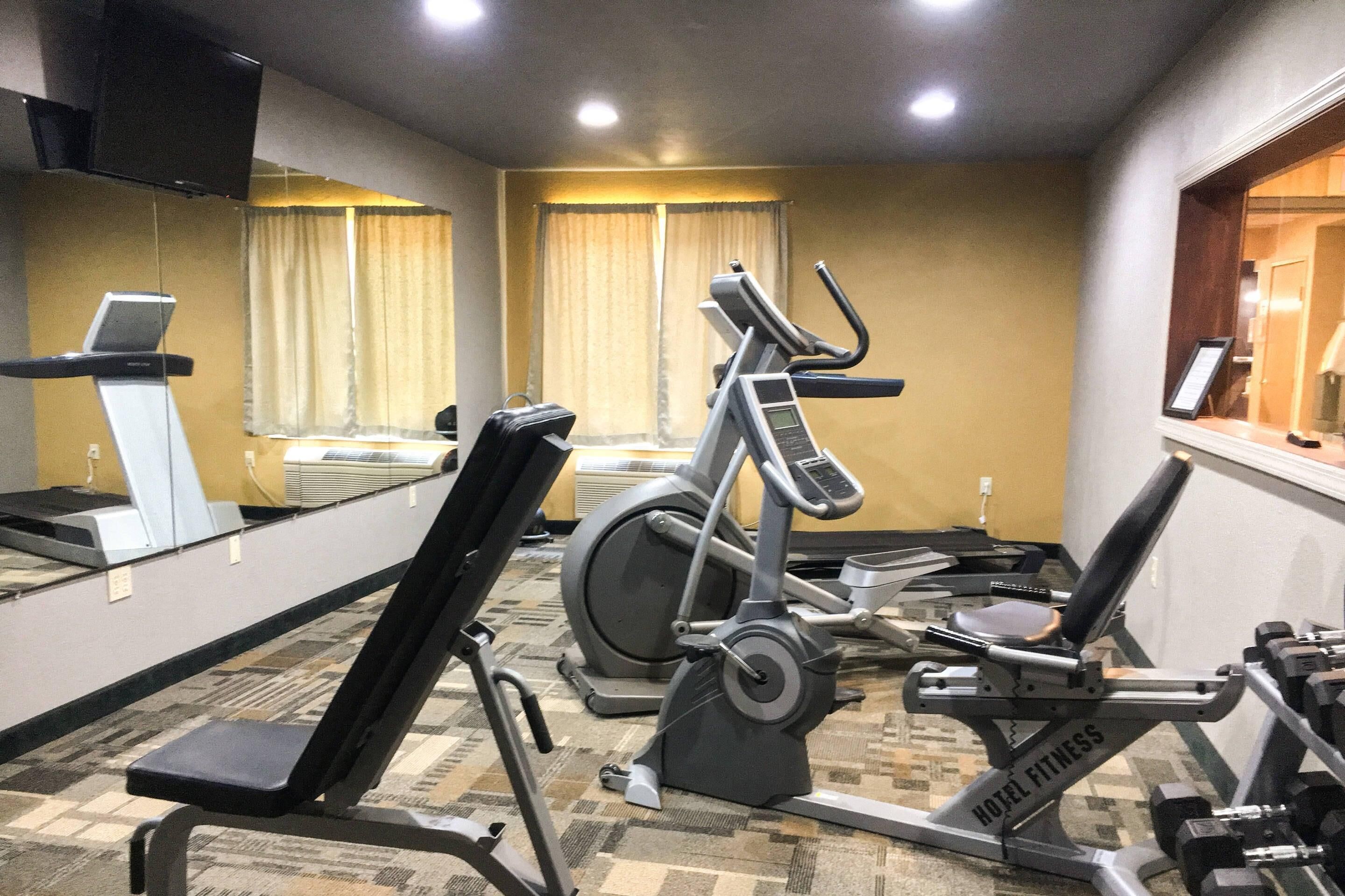 Un gimnasio de hotel con equipo de ejercicio, una cinta de correr, una bicicleta estática y un banco para pesas.