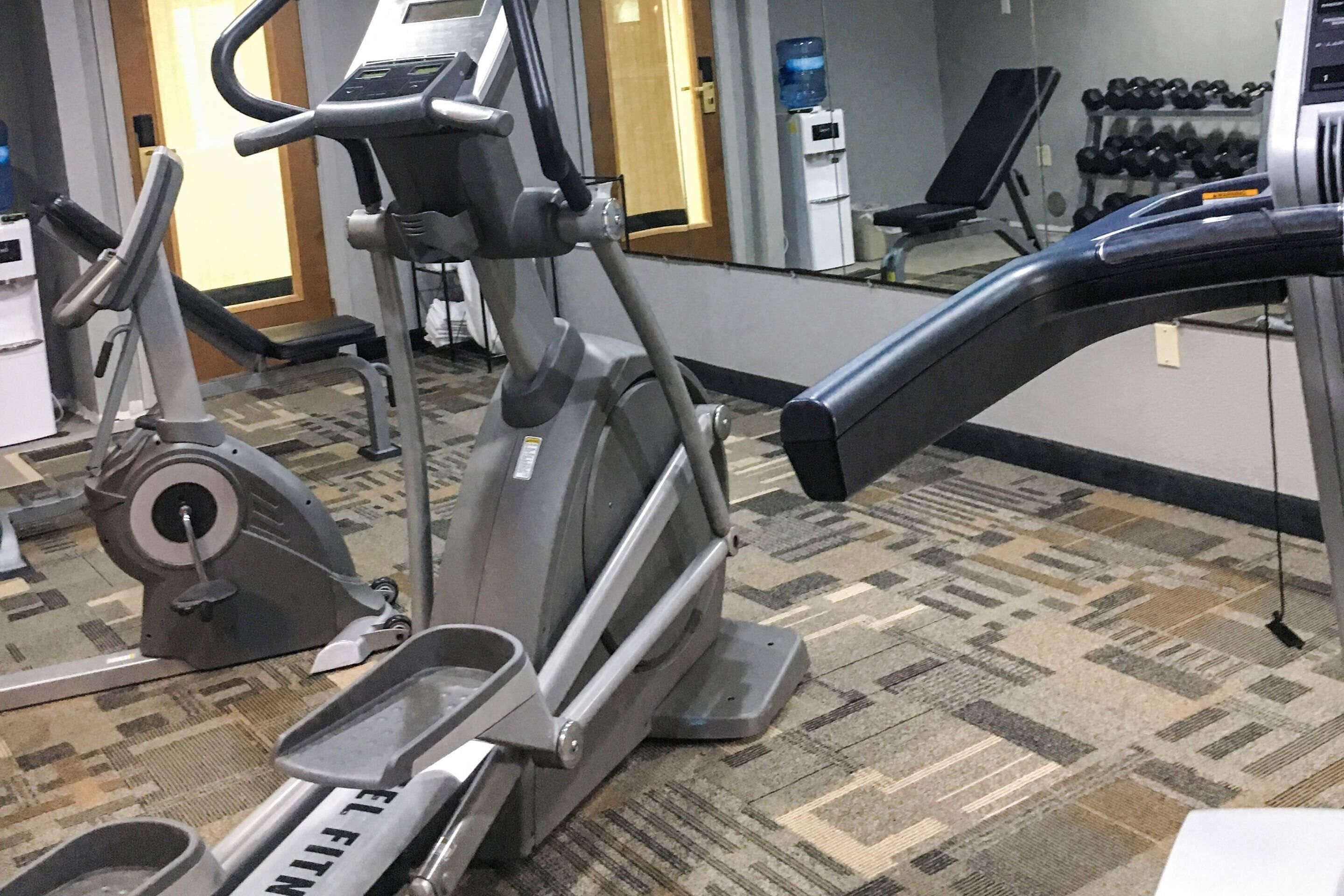 Un área de ejercicios con máquinas de cardio, un dispensador de agua y un estante con mancuernas.