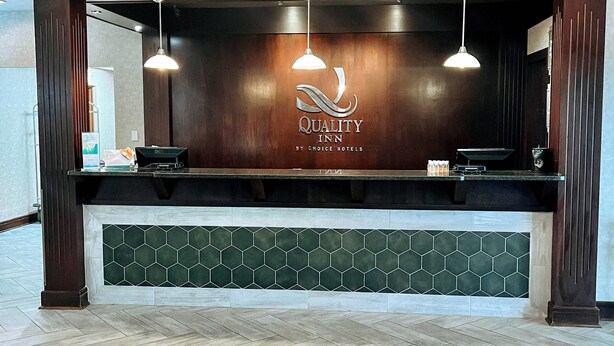 A reception desk with a logo for Quality Inn by Choice Hotels, a wooden counter, and a green-tiled lower section.
