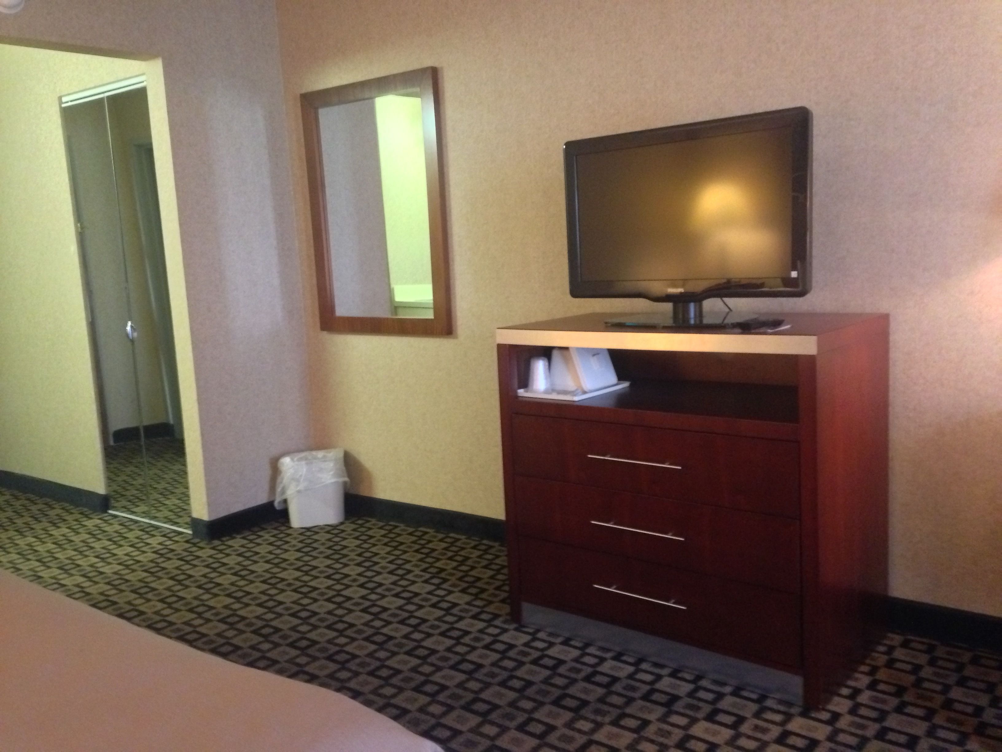 Habitación de hotel con un armario de madera, televisor, espejo y un cesto de basura.