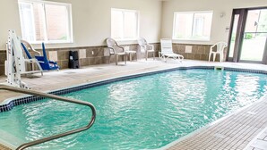 An indoor swimming pool with a tiled floor, a metal pool ladder, and several lounge chairs around the pool area.