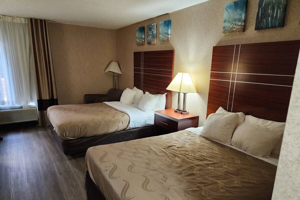 Een hotelkamer met twee bedden, een nachtkastje met lamp, een raam met gordijnen en kunst aan de muur.