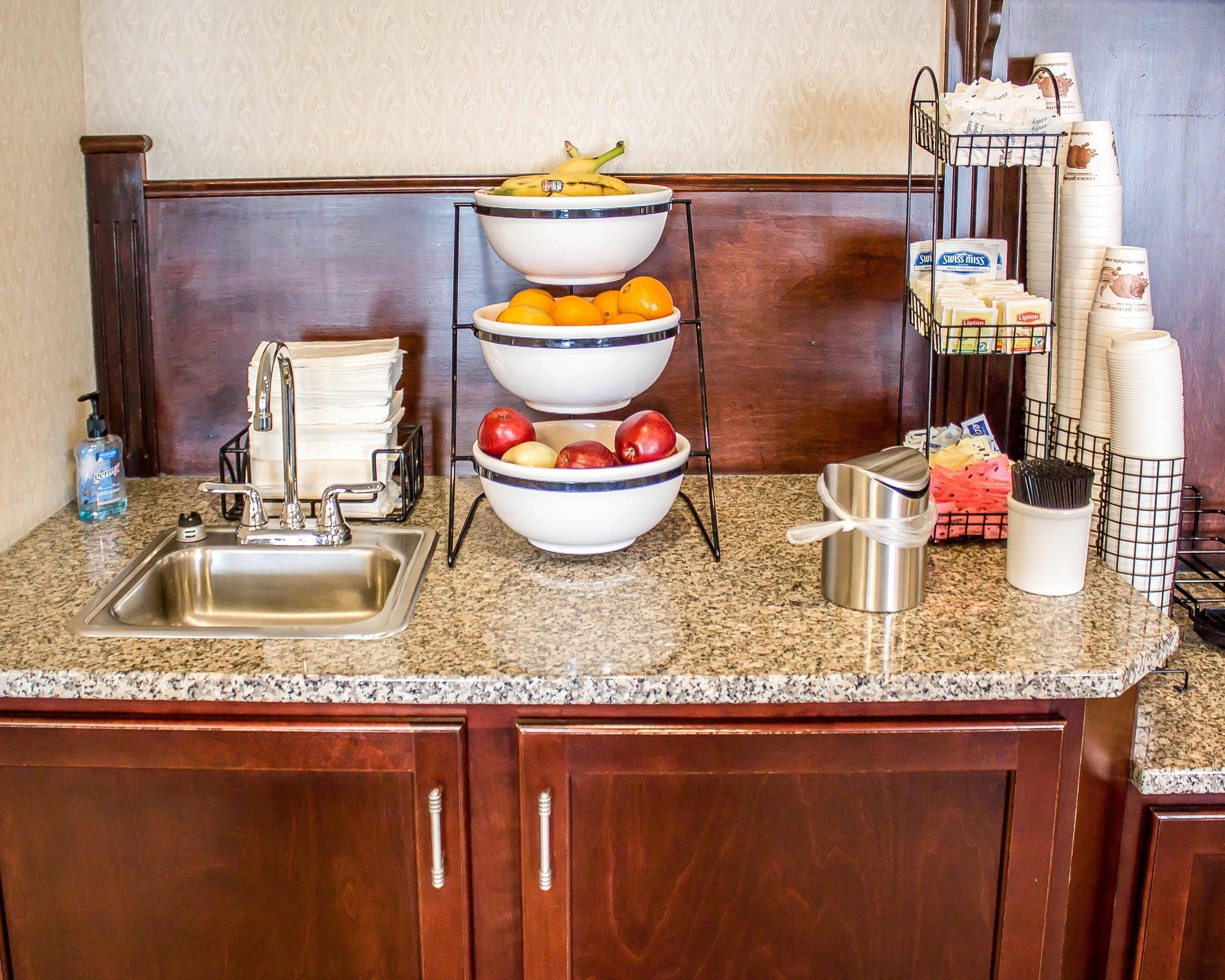 A kitchen with granite countertops, a stainless steel sink, and a three-tiered fruit bowl.
