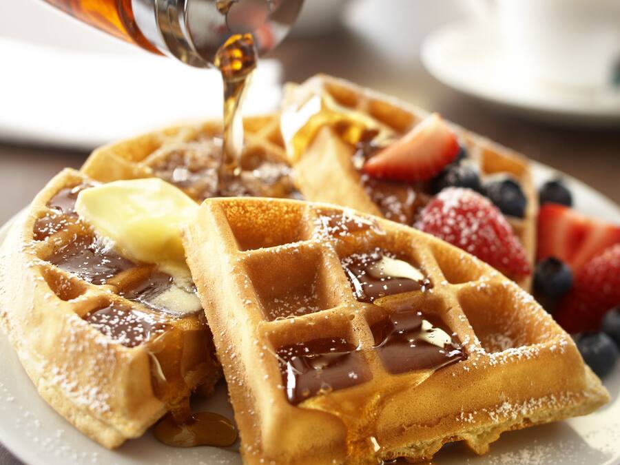Ein Teller mit Waffeln, Sirup, Butter und frischen Beeren.