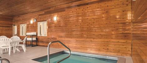 Interior de una cabaña de madera con piscina, sillas de plástico blanco y una mesa.