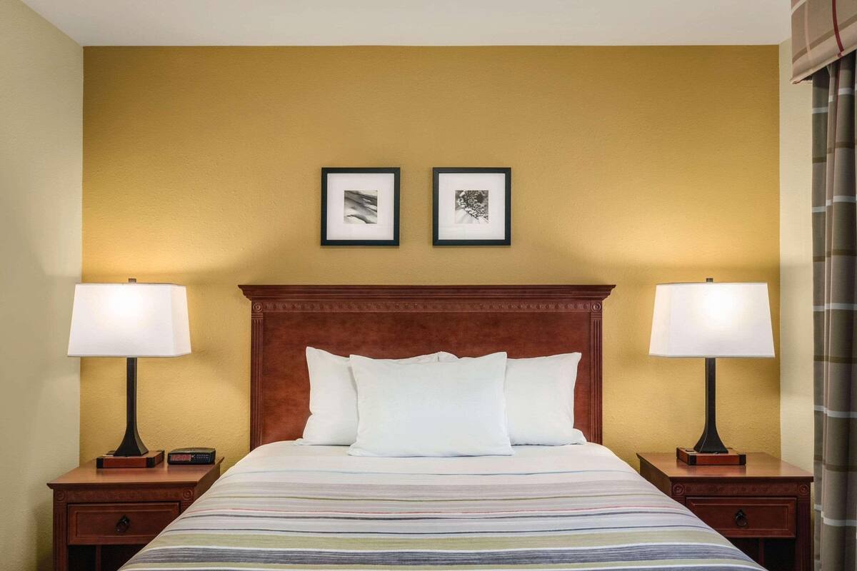 A hotel room with a large bed, two bedside lamps, a wooden headboard, and two framed pictures on the wall.