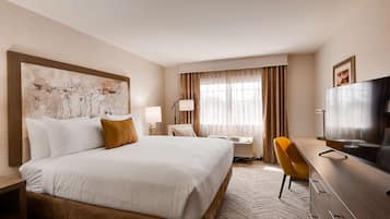 Quarto de hotel com uma cama grande, uma escrivaninha com cadeira, televisão e janela com cortinas.