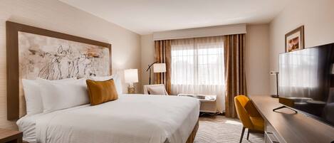 A hotel room with a large bed, a desk with a chair, a television, and a window with curtains.