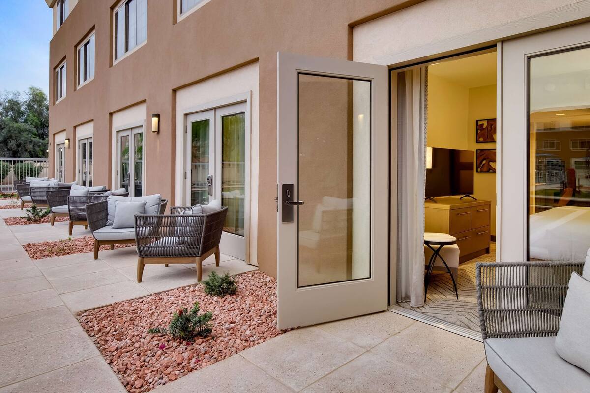 L’extérieur d’un hôtel, avec un patio aménagé de meubles en osier et une porte vitrée donnant sur l’intérieur.
