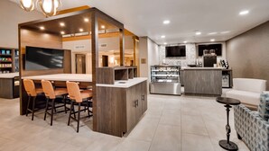 A modern hotel lobby with a bar area, seating, a coffee machine, and a TV.