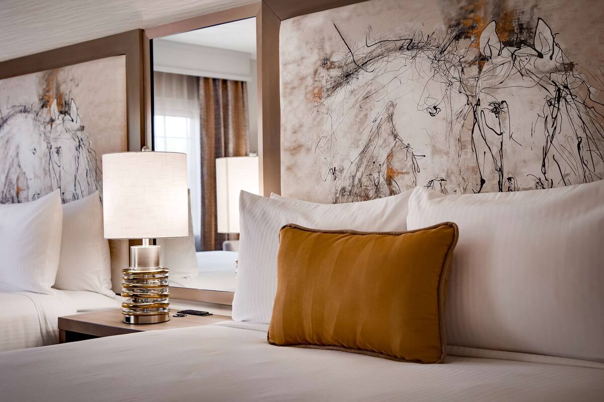 Une chambre d’hôtel avec deux lits, une lampe moderne et des œuvres d’art abstraites accrochées aux murs.