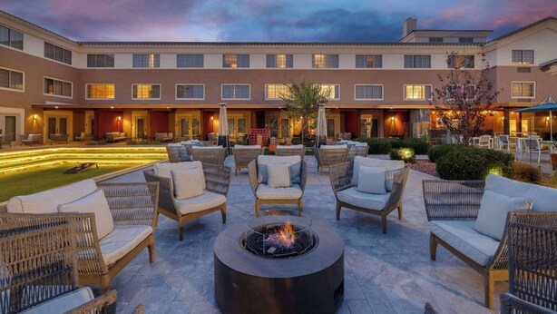 A courtyard with outdoor seating and a fire pit, surrounded by a building with multiple windows and doors.