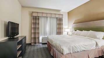 A hotel room with a bed, a TV on a stand, a desk, and a window with curtains.
