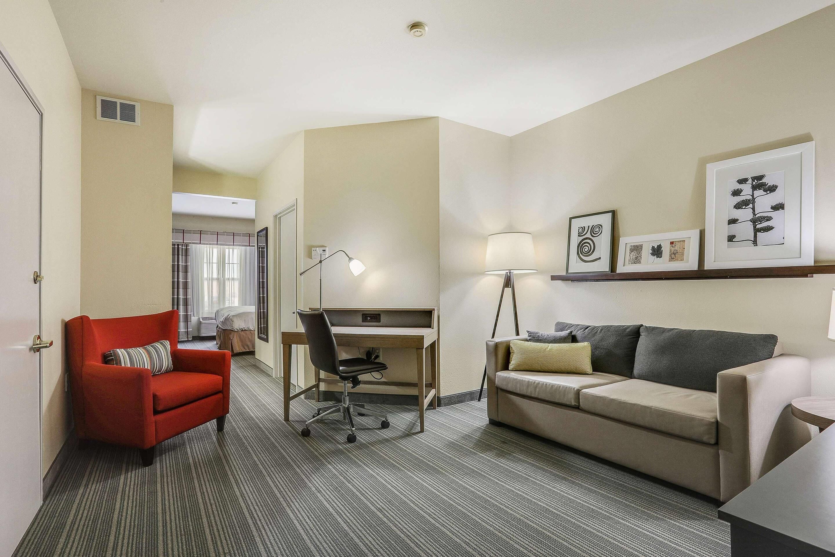 Habitación de hotel con escritorio, un sillón rojo, sofá y cuadros en la pared.