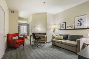 Habitación de hotel con escritorio, un sillón rojo, sofá y cuadros en la pared.