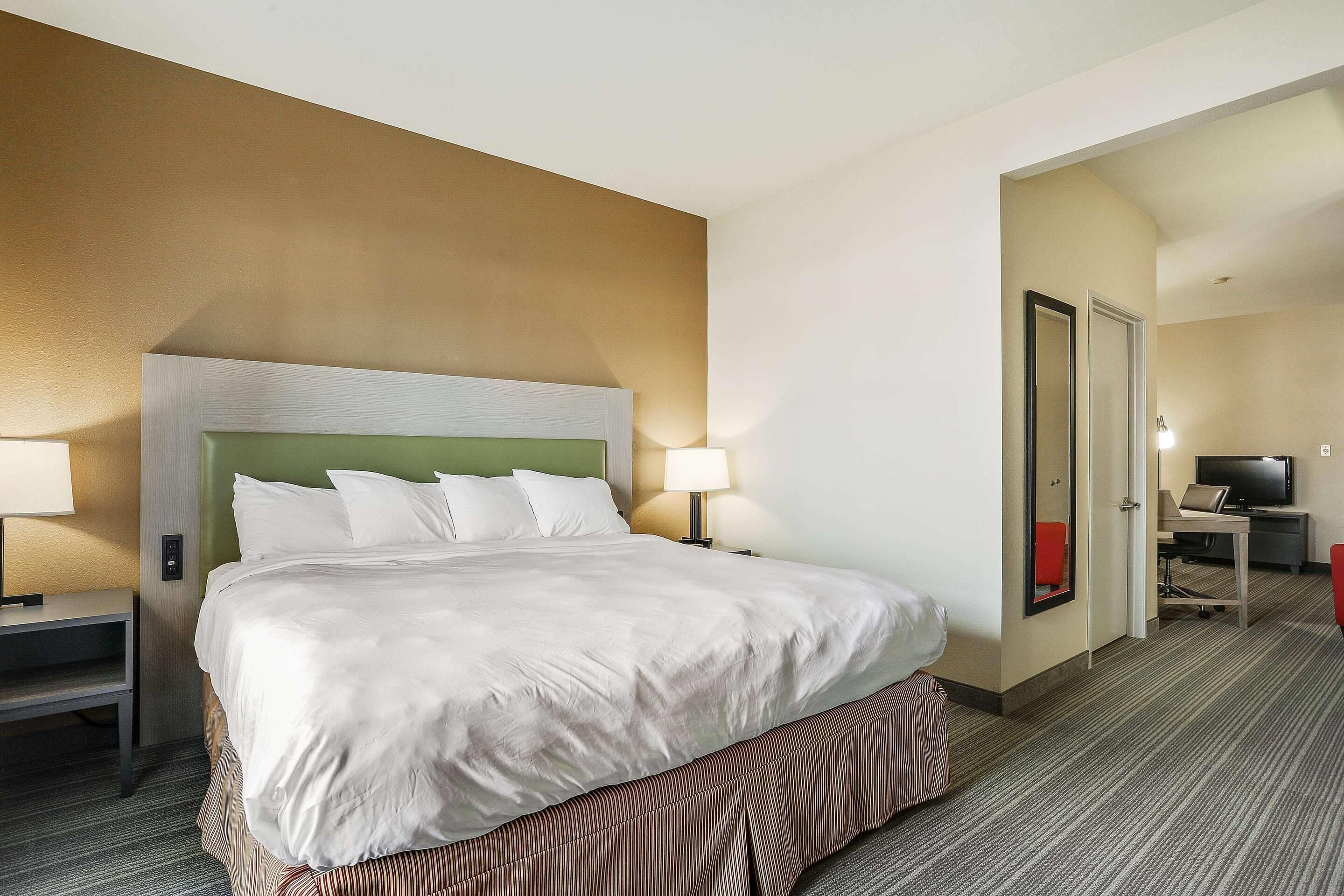 A hotel room with a large bed, bedside tables, a desk with a chair, and a television.