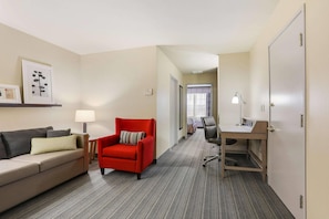 A hotel room with a sofa, a red armchair, a desk, and a lamp. - Country Inn & Suites by Radisson, Green Bay, WI (Green Bay)