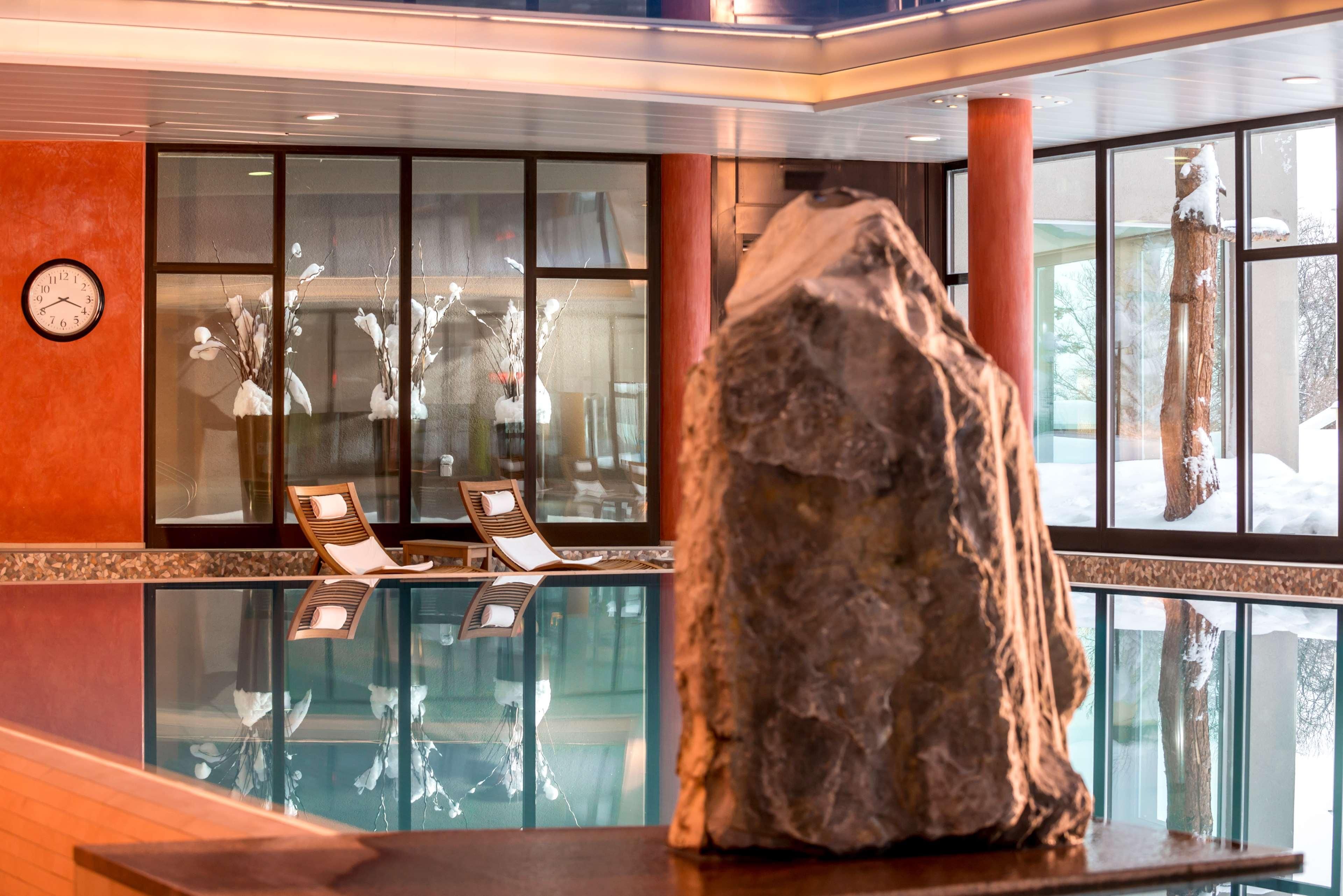 Eine Lobby mit einem Glaspool, zwei Liegestühlen, einer großen Felsformation und einer Wanduhr.