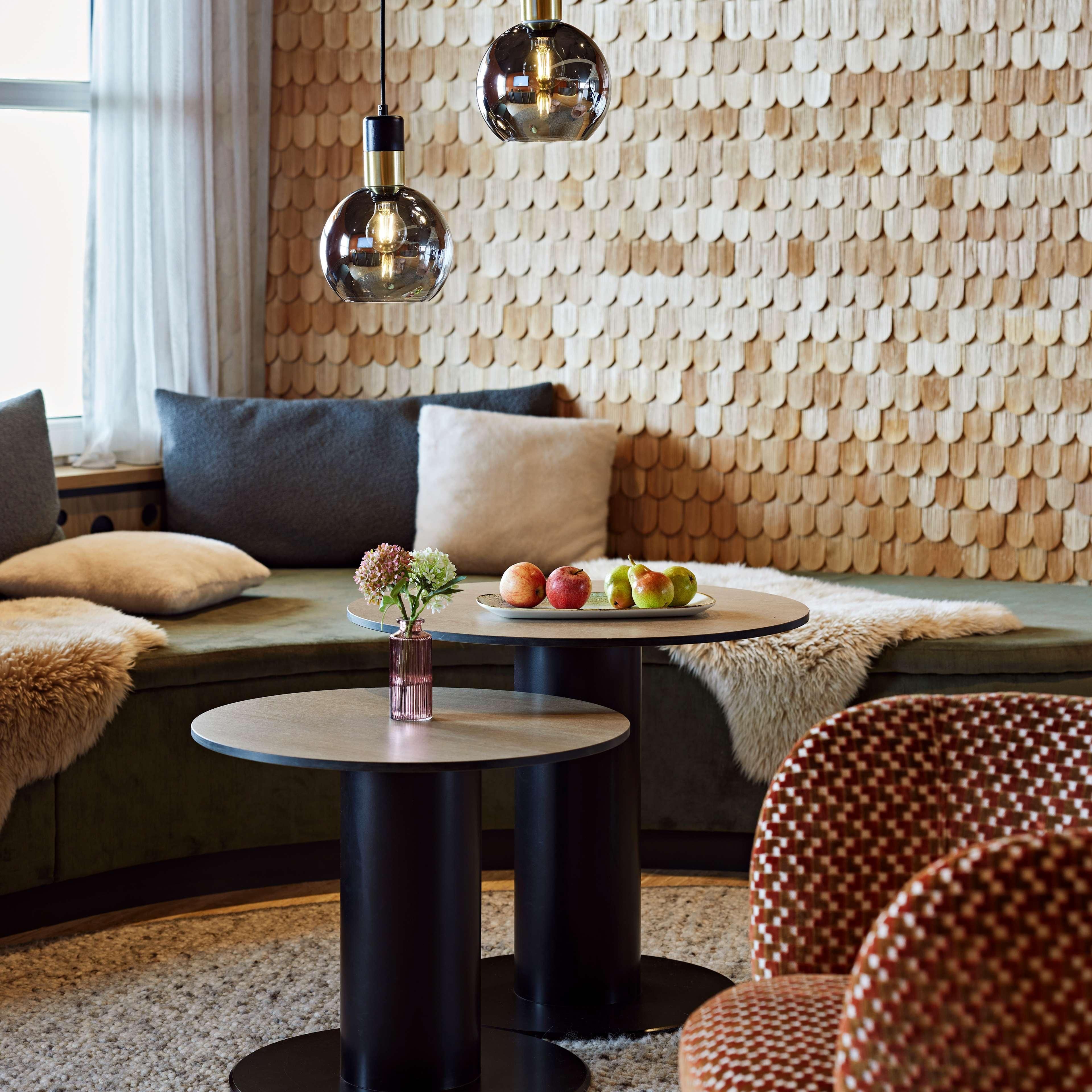 A modern living room with a round coffee table, a sofa with cushions, a wall with a wooden pattern, and hanging pendant lights.