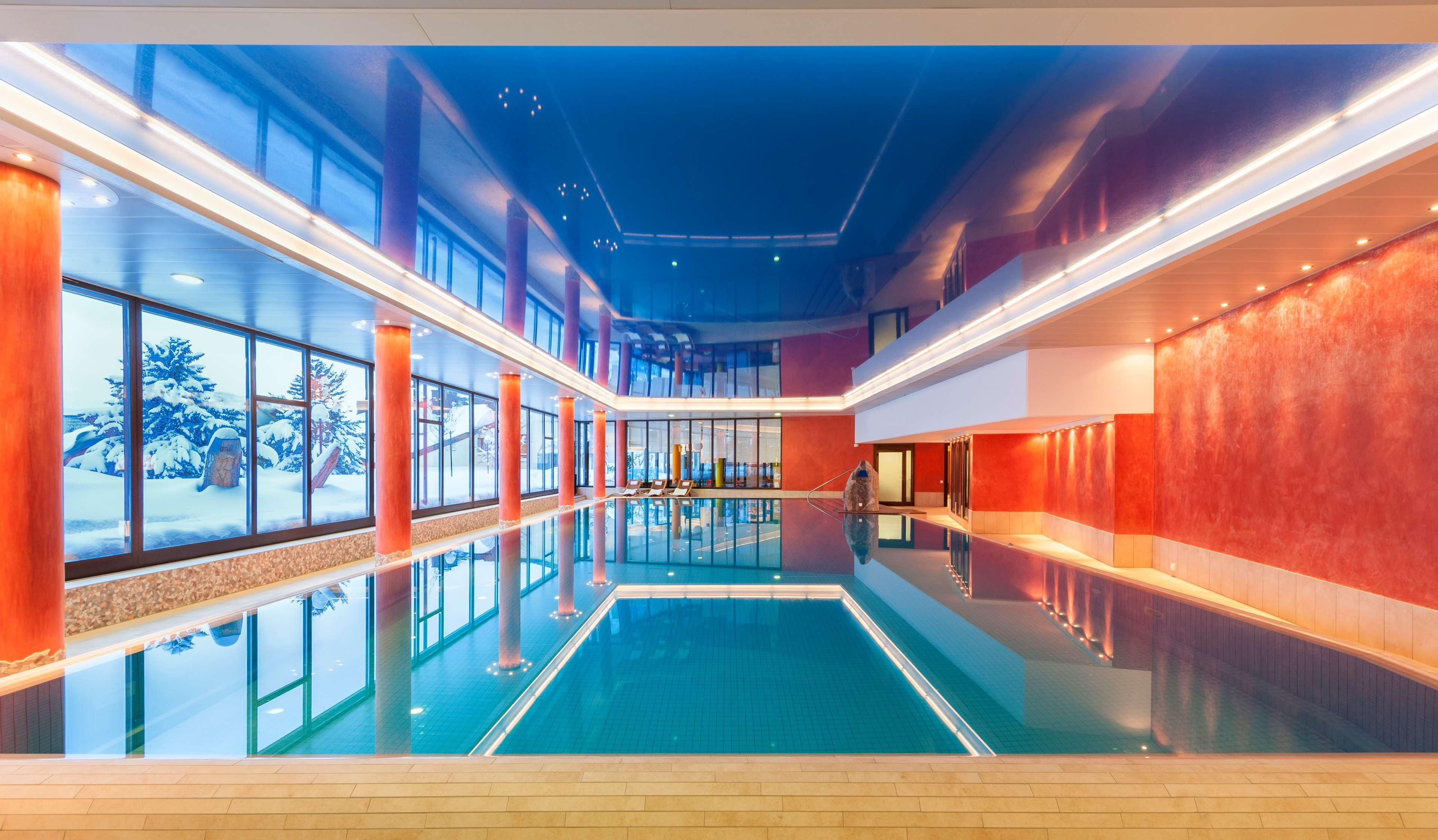 A large indoor swimming pool with glass walls and a view of a snowy landscape.