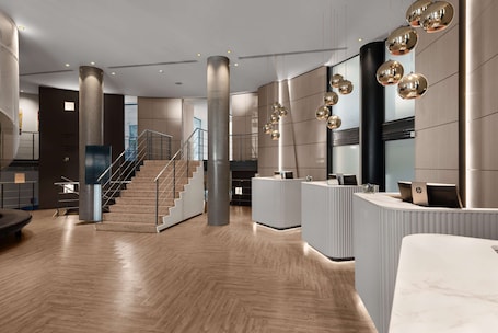 A modern reception area with a wooden floor, a staircase, and a reception desk with computers.