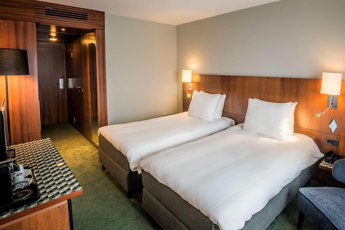 Habitación de hotel con dos camas, un escritorio con cafetera, un teléfono y una pequeña mesa con camino de mesa a cuadros.