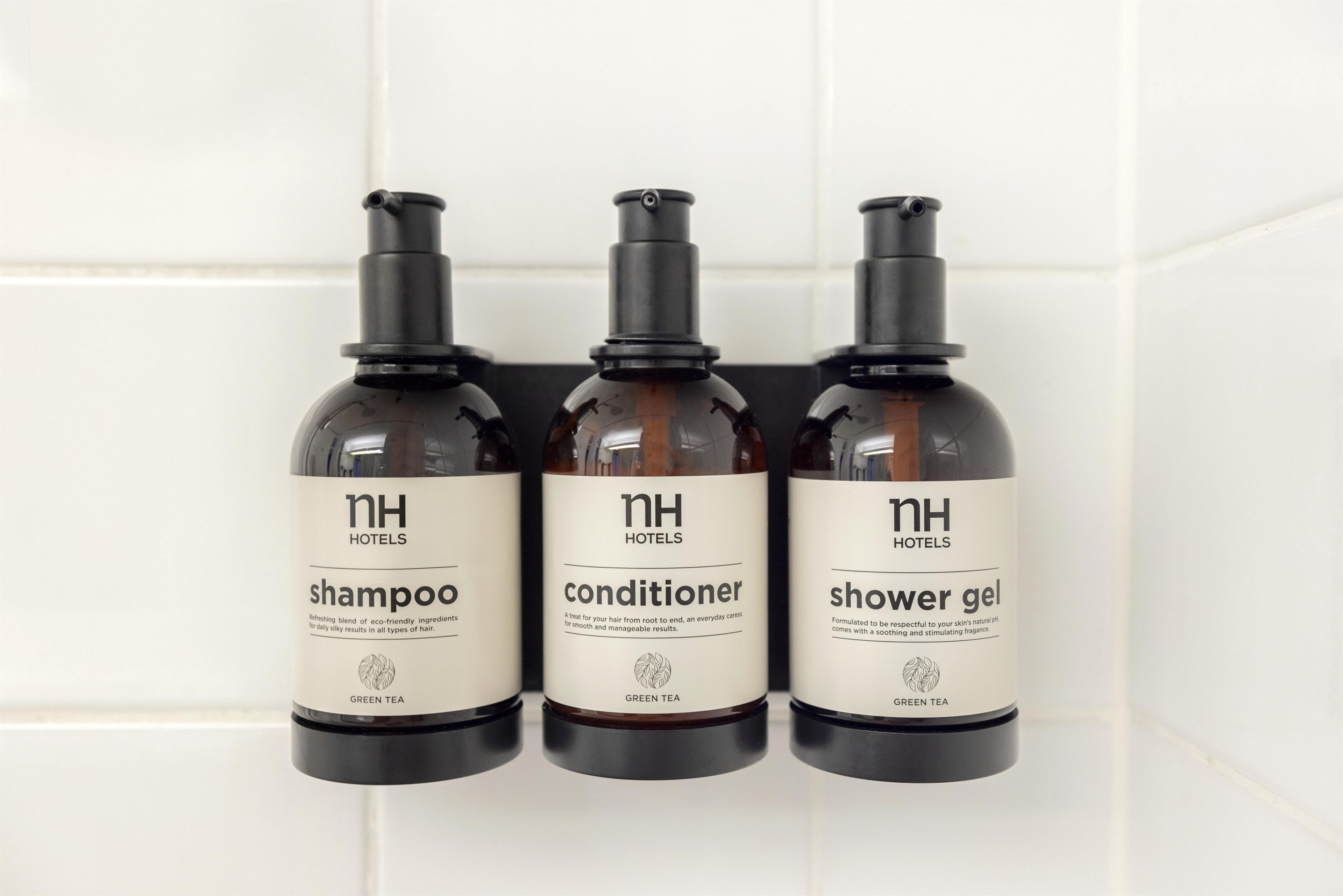 Three bottles of hotel toiletries on a white tiled wall.