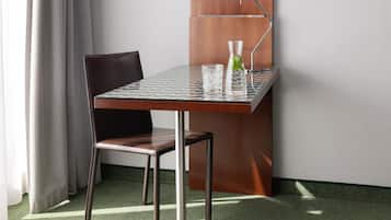 Een kleine, moderne kamer met een tafel met glazen blad, een stoel en een waterkan met een muntblaadje.