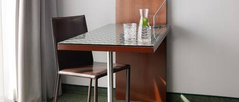 Una habitación pequeña y moderna con una mesa de vidrio, una silla y una jarrón con una hoja de menta.