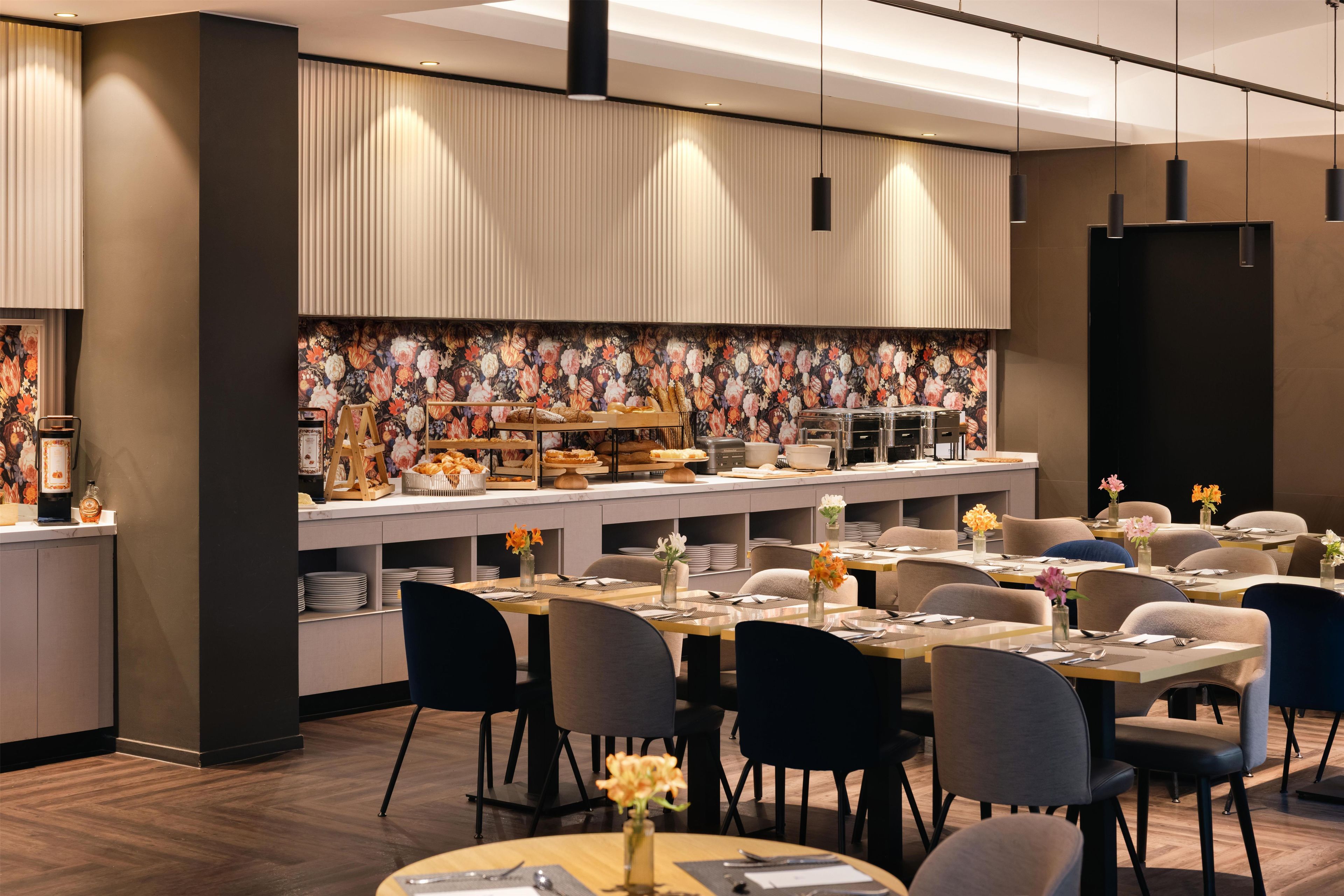 A modern dining area with a buffet setup, including a variety of food items and a floral wall mural.