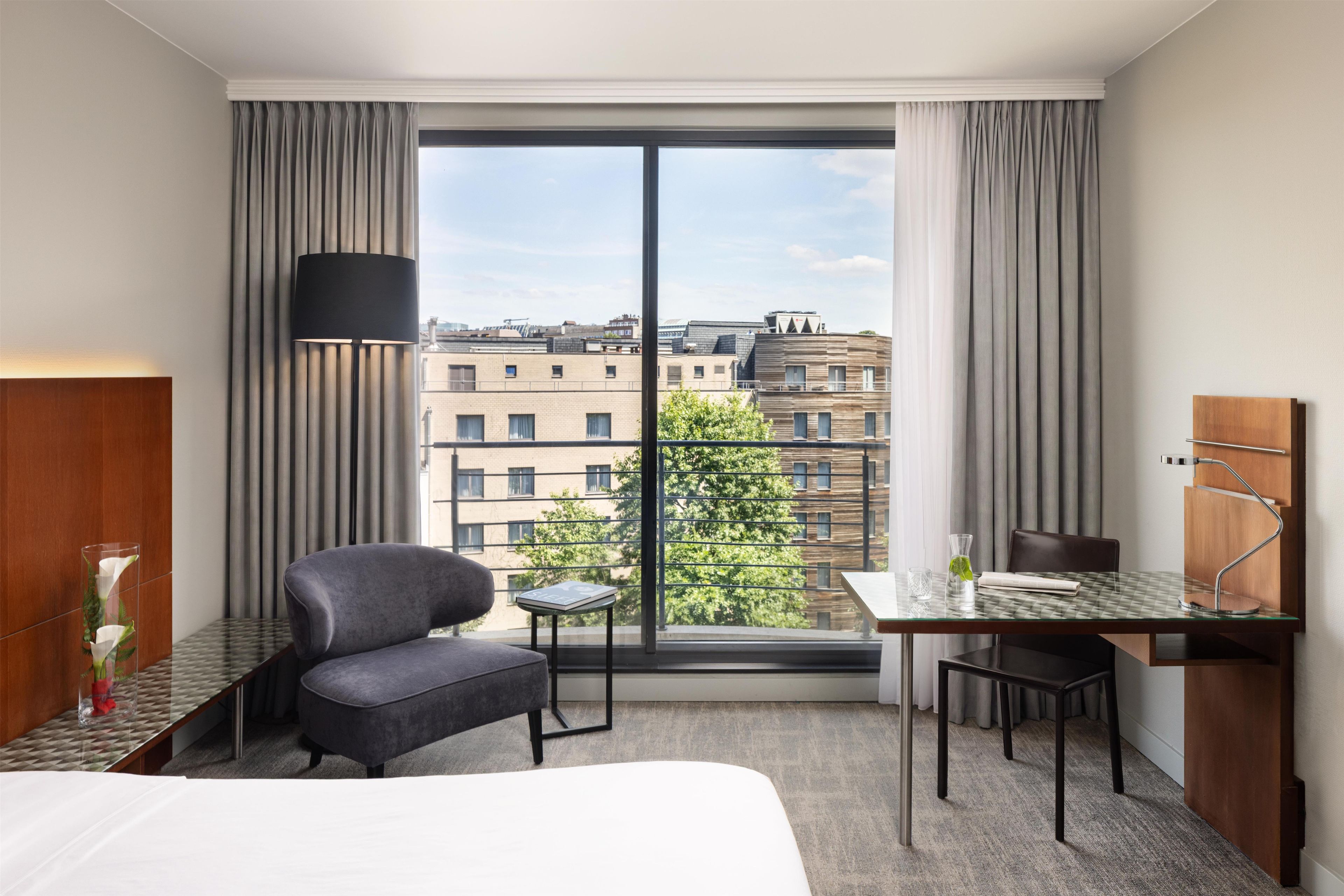 Habitación de hotel con cama, escritorio, silla, lámpara y vista de la ciudad.