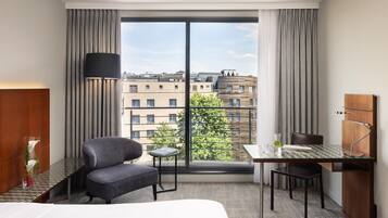 Habitación de hotel con cama, escritorio, silla, lámpara y vista de la ciudad.