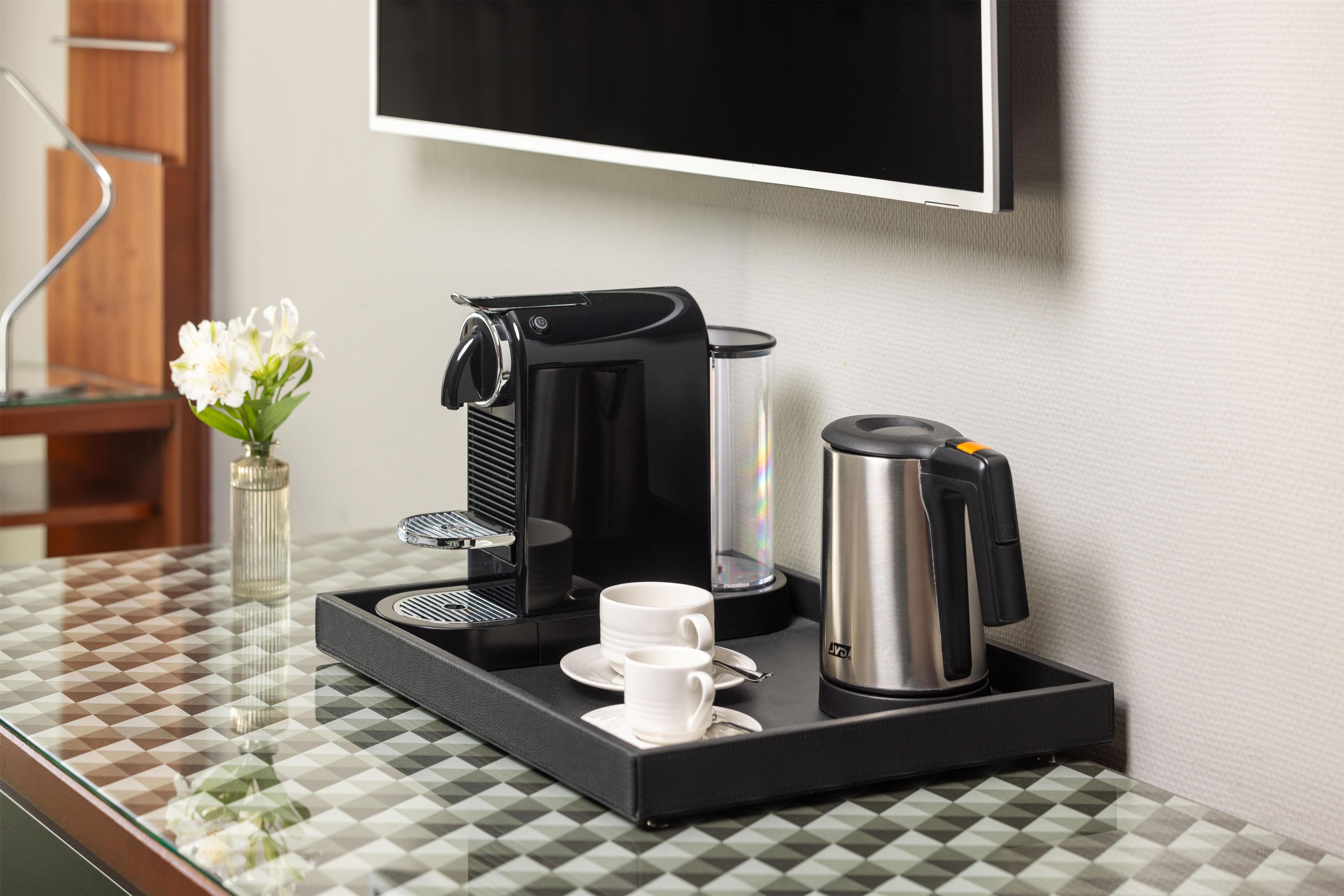 A coffee station with a coffee maker, a water dispenser, a thermos, and a tray with cups and saucers.