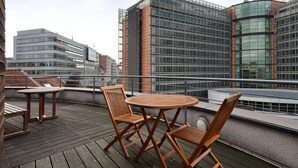 Terraza en la azotea con mobiliario de madera y vistas a edificios modernos.