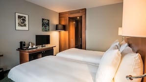 Habitación de hotel con dos camas, un escritorio con televisor, cafetera y armario.