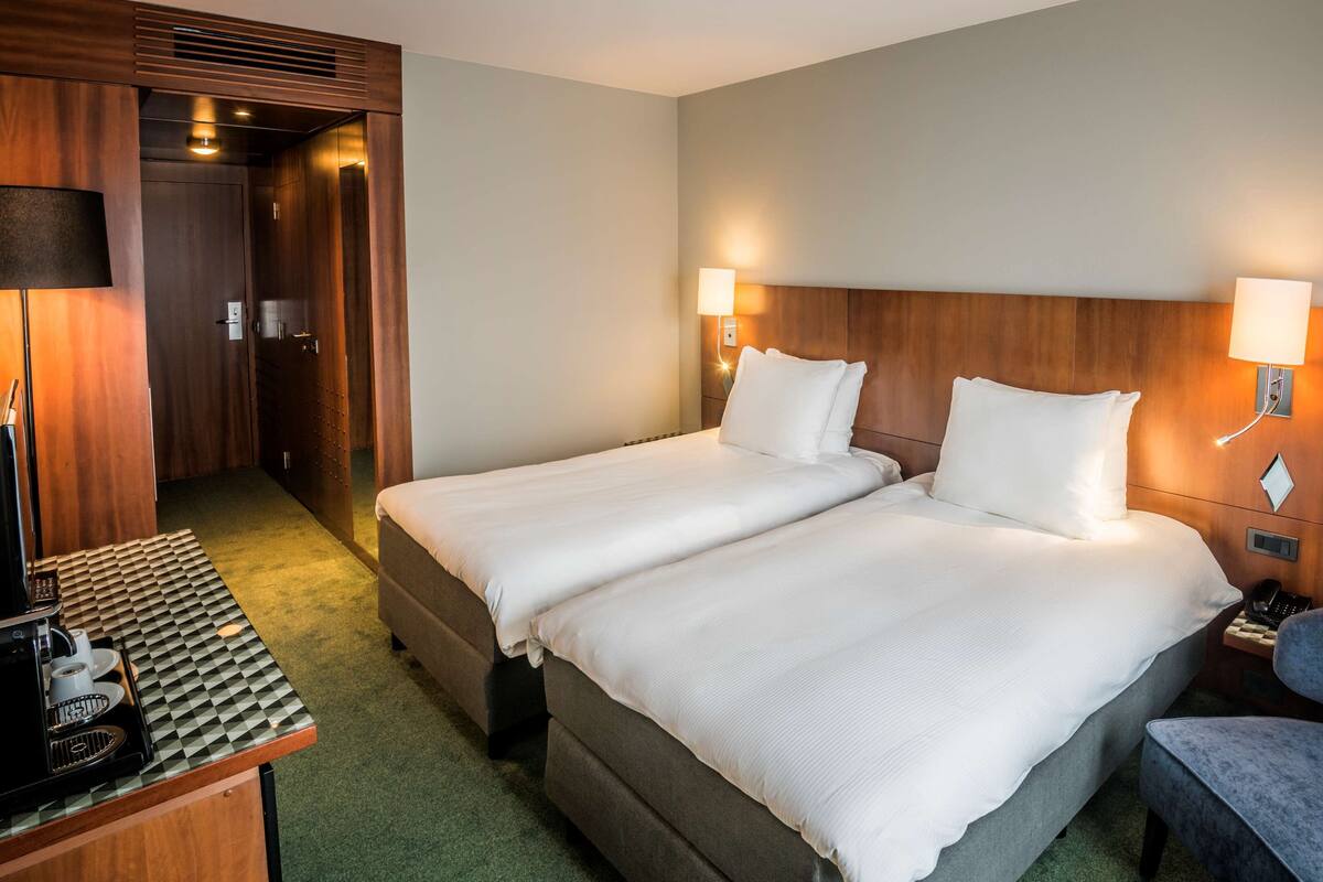 A hotel room with two beds, a desk with a coffee machine, and a chair.