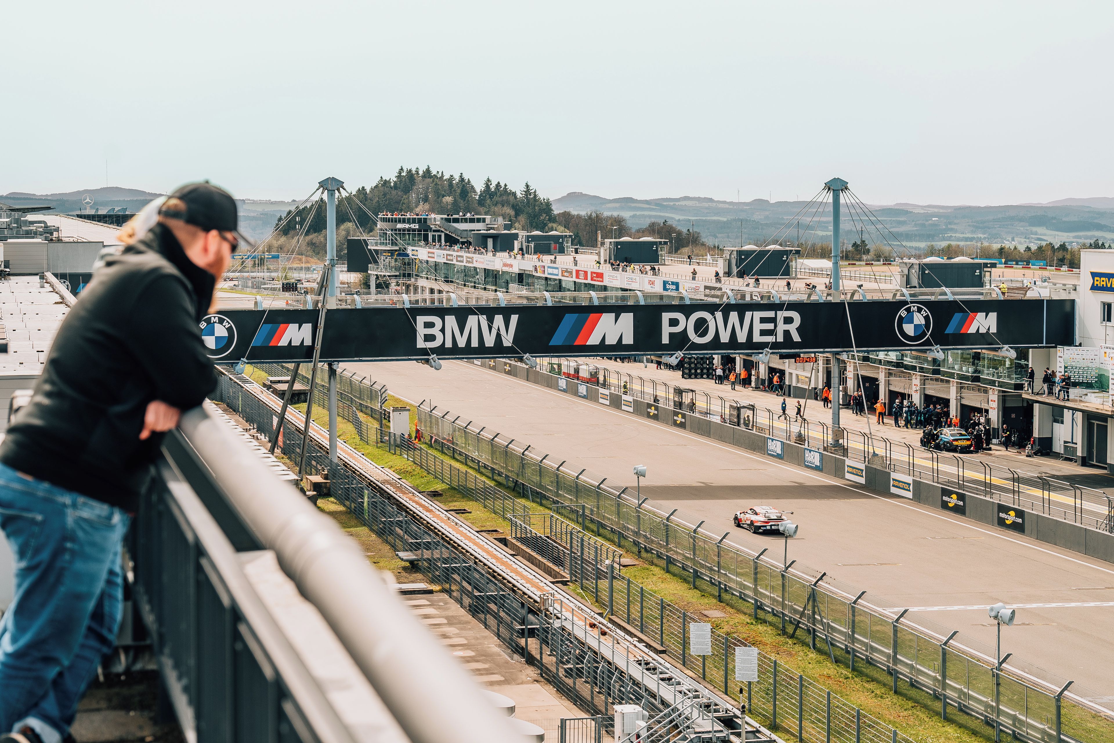A race track with a BMW Power banner, spectator stands, and a clear sky.