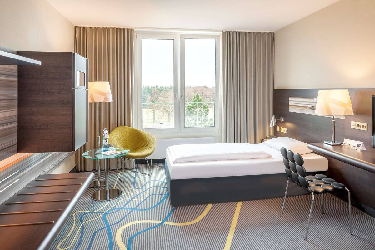 Una habitación de hotel con cama, escritorio, silla, mesita y ventana con cortinas.