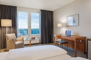 Habitación de hotel con cama, escritorio con computadora portátil, silla, mesa con fruta y ventana con cortinas.