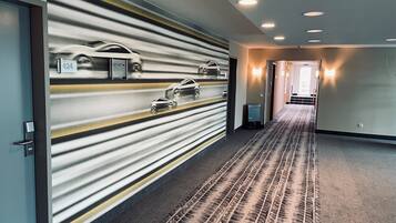 A hotel hallway with a patterned wall, a carpeted floor, and a door with a number sign.