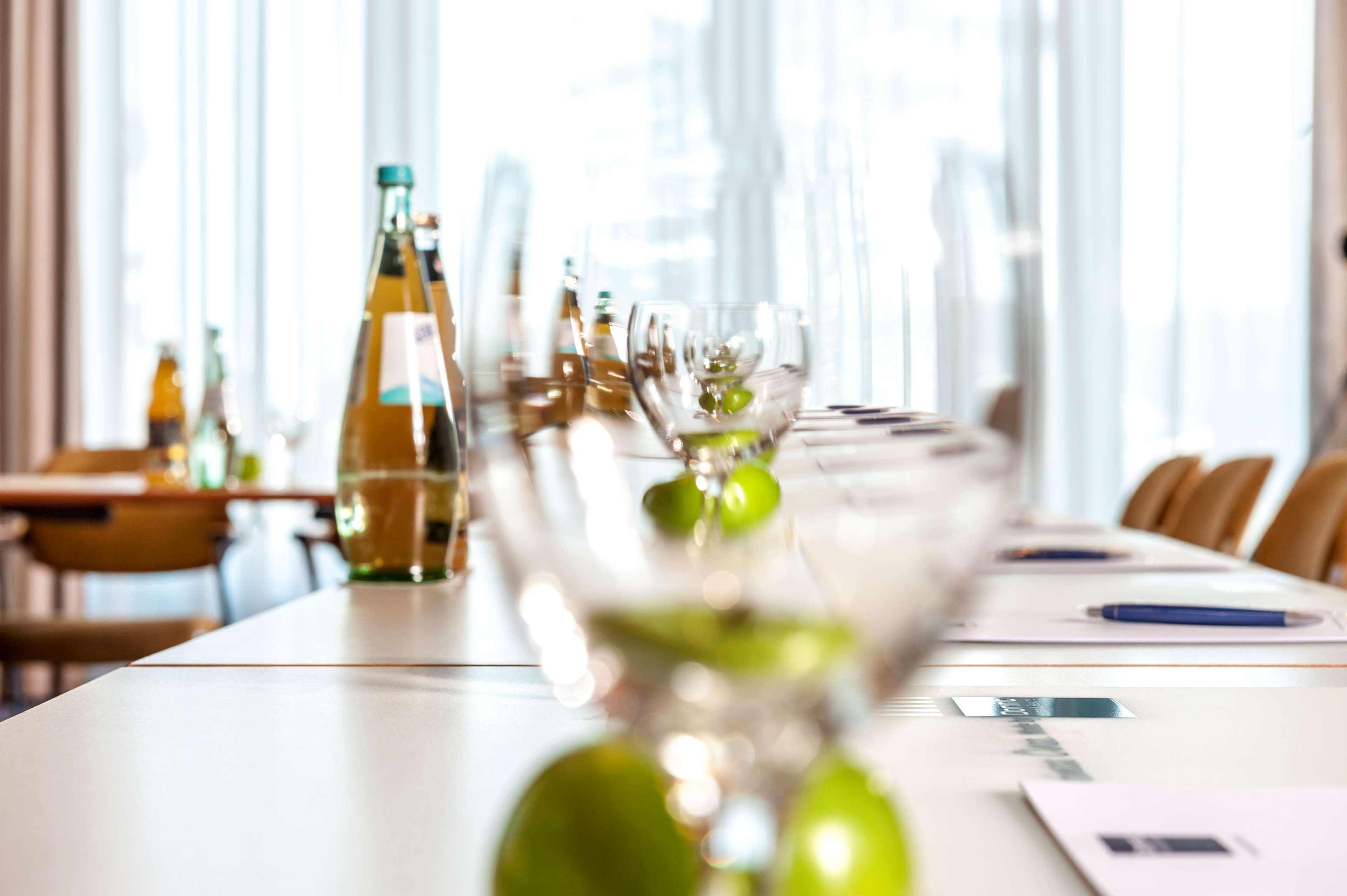 A conference table with a bottle of olive oil, a glass with a green garnish, and a pen on a notepad.