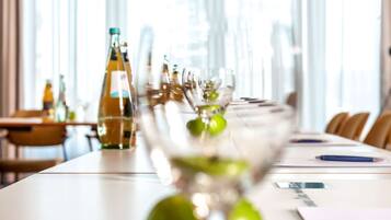 A conference table with a bottle of olive oil, a glass with a green garnish, and a pen on a notepad.